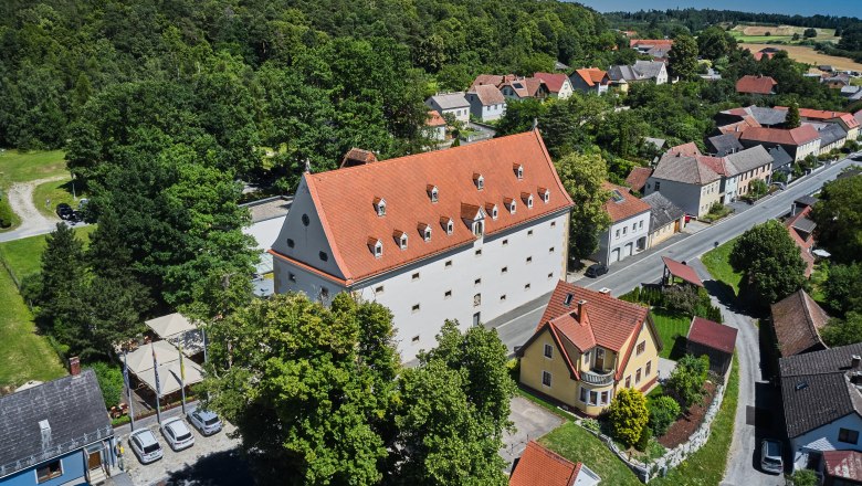 Hotel Schüttkasten, © Franz Gleiss Luftaufnahme eines großen Gebäudes mit rotem Dach, umgeben von Bäumen und kleineren Häusern in einer ländlichen Gegend.