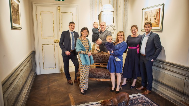 Familie Pichler, © Familie Pichler Eine Gruppe von Menschen posiert in einem eleganten Raum mit einem Hund im Vordergrund.