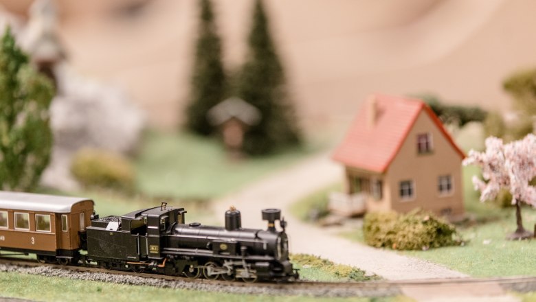 Modellbahn, © schwarz-koenig.at Modellbahn mit Dampflok und Waggon auf einer Miniaturlandschaft mit Haus und Bäumen.