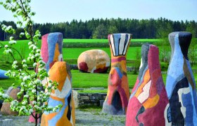 Bunte Skulpturen in einer grünen Landschaft mit Bäumen im Hintergrund.