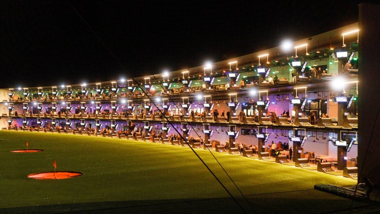 Beeindruckende Abendstimmung bei Topgolf mit beleuchteten Abschlagpl&auml;tzen auf mehreren Ebenen und zahlreichen G&auml;sten beim gemeinsamen Spielen und Genie&szlig;en.