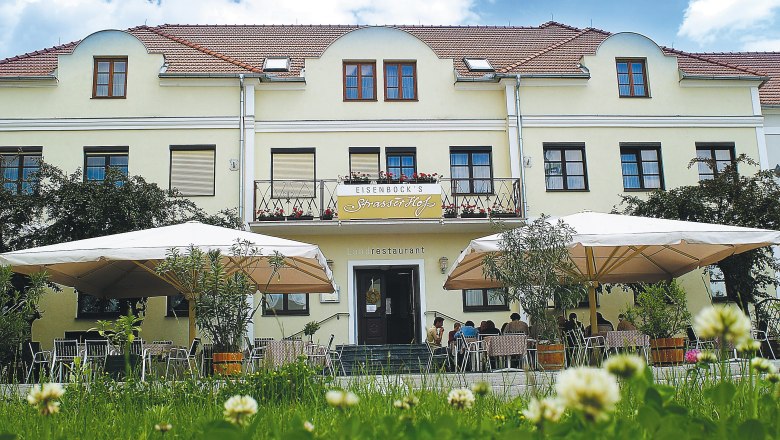 Außenansicht eines gelben Gebäudes mit Terrasse und Sonnenschirmen.