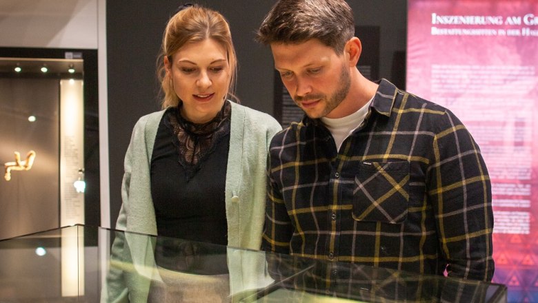 Zwei Personen betrachten Artefakte in einer Glasvitrine im Museum.