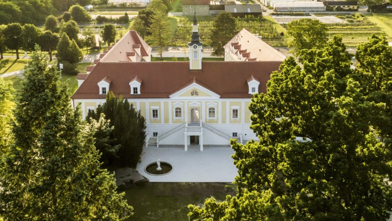 Luftaufnahme eines gro&szlig;en, gelben Geb&auml;udes mit rotem Dach und Turm, umgeben von B&auml;umen und Gr&uuml;nfl&auml;chen.