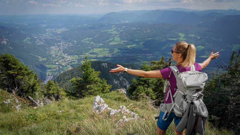 Eine Frau mit Rucksack genie&szlig;t die Aussicht auf ein Tal von einem Berg aus.