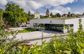 Modernes Gebäude des Sconariums mit Kirche im Hintergrund.