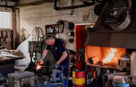 Ein Schmied arbeitet in einer Werkstatt mit einem brennenden Schmiedefeuer.