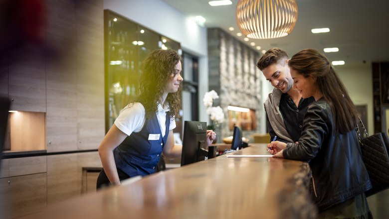 Ein Paar checkt an der Rezeption eines Hotels ein, während eine Rezeptionistin ihnen hilft.