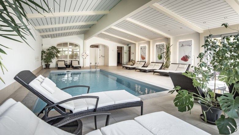 Innenansicht eines Hotelpools mit Liegestühlen und Pflanzen.