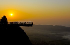 Skywalk bei Sonnenuntergang mit Blick auf eine Landschaft und Berge im Hintergrund.