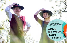 Zwei Personen mit H&uuml;ten in einem bl&uuml;henden Garten, Plakat f&uuml;r N&Ouml; Landesausstellung 2026.