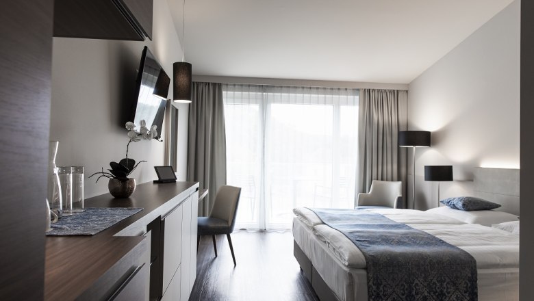 Modernes Hotelzimmer mit Doppelbett, Fernseher, Schreibtisch und Balkon.