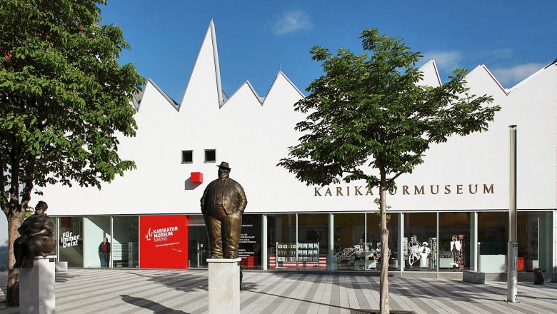 Außenansicht des Karikaturmuseums Krems mit Statuen und Bäumen.