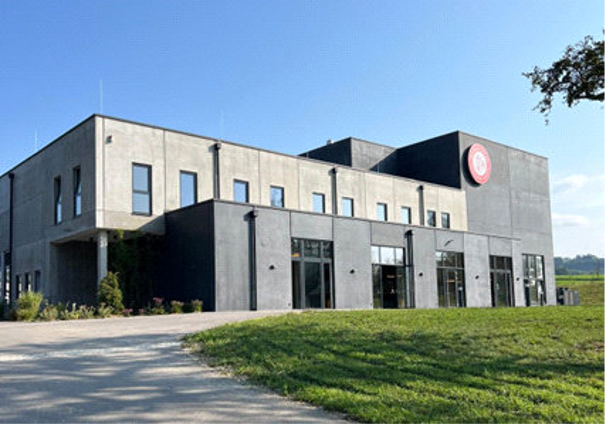 Modernes Geb&auml;ude der Destillerie Farthofer mit grauer Fassade und gro&szlig;en Fenstern, umgeben von gr&uuml;ner Wiese und blauem Himmel.