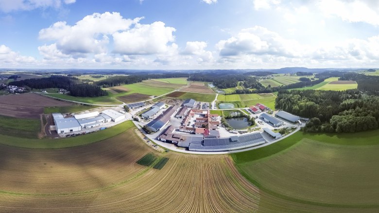 Luftaufnahme einer ländlichen Landschaft mit Feldern, Gebäuden und Wäldern unter einem bewölkten Himmel.