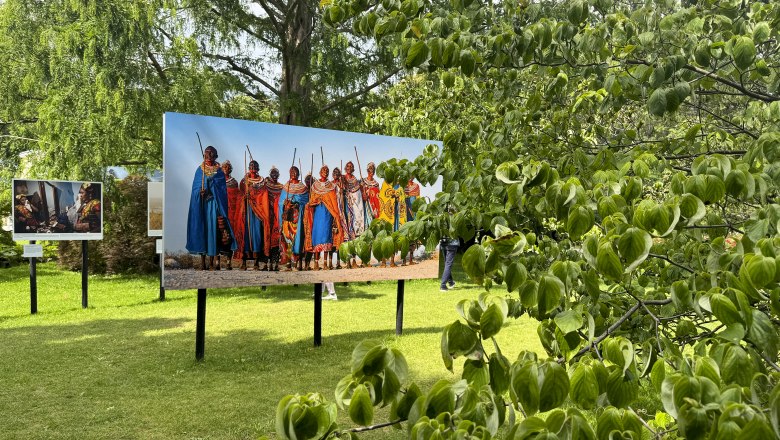 Outdoor-Fotoausstellung mit Bildern von Menschen in traditioneller Kleidung auf einer Wiese.