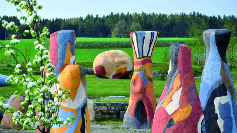 Bunte Skulpturen in einer gr&uuml;nen Landschaft mit B&auml;umen im Hintergrund.