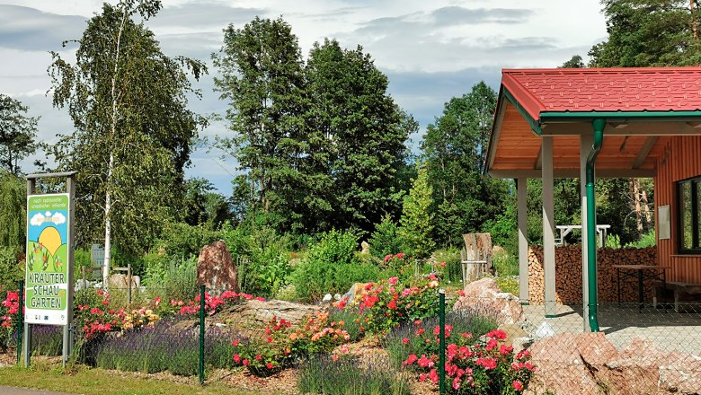 Ein Kr&auml;uterschaugarten mit bunten Blumen, B&auml;umen und einem Geb&auml;ude mit rotem Dach.