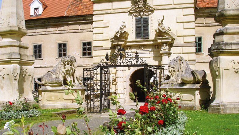 Eingang von Schloss Greillenstein mit Löwenstatuen und blühenden Rosen im Vordergrund.
