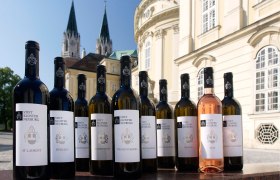 Weinflaschen des Stift Klosterneuburg vor einem historischen Gebäude.