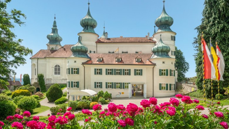 Schloss Artstetten mit blühenden Blumen im Vordergrund und Flaggen rechts.