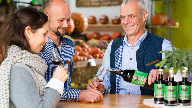 Drei Personen bei einer Weinverkostung in einem Gesch&auml;ft mit K&uuml;rbissen im Hintergrund.