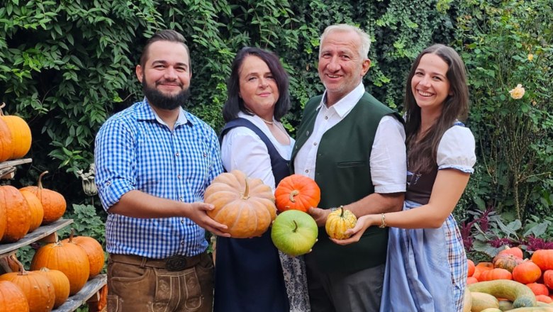 Vier Personen halten K&uuml;rbisse in einem Garten mit vielen K&uuml;rbissen.