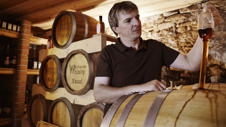 Ein Mann verkostet Whisky in einem Lagerraum mit Fässern.