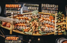 Ein großes Sushi-Buffet auf einem Holztablett mit verschiedenen Sushi-Varianten, dekoriert mit Gurken und Ingwer.