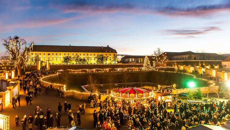 Weihnachtsmarkt im Schloss Hof bei D&auml;mmerung mit Lichtern und Menschen.