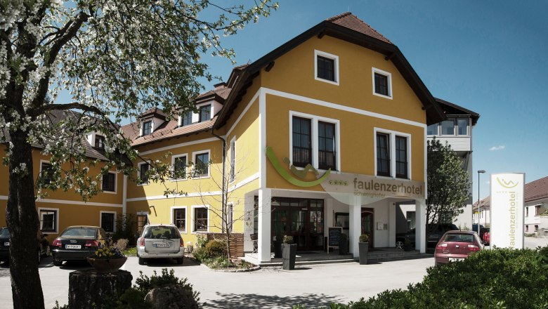 Gelbes Hotelgebäude mit Autos im Vordergrund und blühendem Baum.