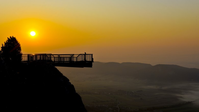 Skywalk bei Sonnenuntergang mit Blick auf eine Landschaft und Berge im Hintergrund.