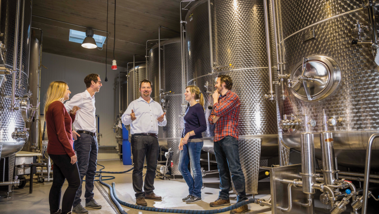 Gruppe von Menschen in einer Brauerei mit großen Metalltanks.