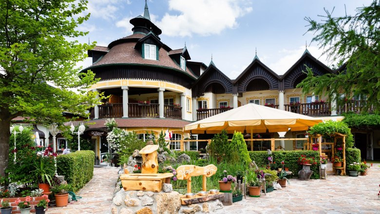 Ein traditionelles Geb&auml;ude mit Holzbalkonen und einem Garten voller Pflanzen und Blumen.