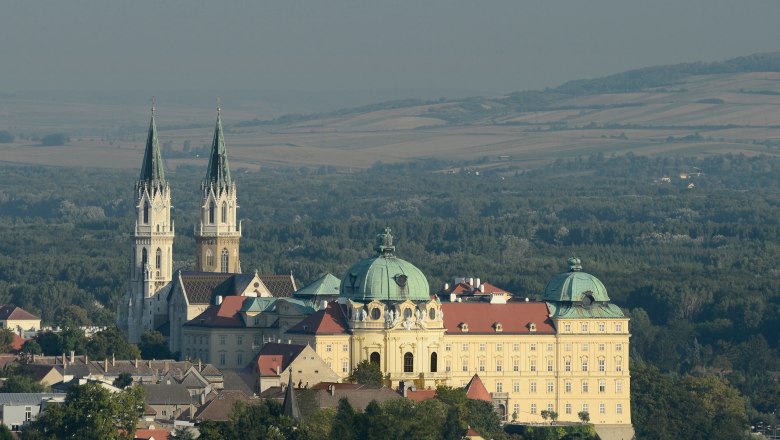 Luftaufnahme des Stifts Klosterneuburg mit zwei Kirchtürmen und umliegender Landschaft.