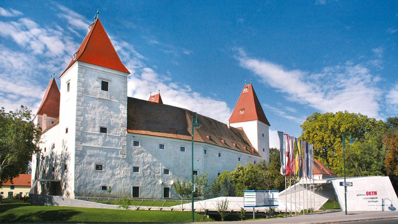Schloss Orth mit roten Dächern und Fahnen im Vordergrund.