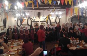 Menschen in mittelalterlicher Kleidung bei einem Festmahl in einem dekorierten Raum.