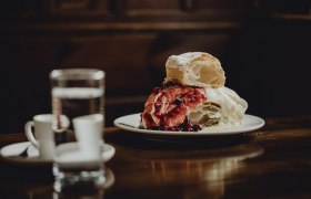 Ein Teller mit Strudel und Beeren, daneben ein Glas Wasser und zwei Espressotassen auf einem Holztisch.