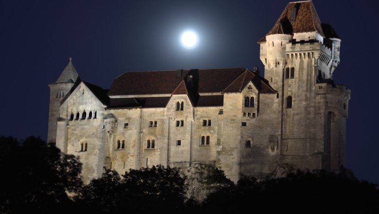 Burg Liechtenstein bei Nacht mit Vollmond im Hintergrund.
