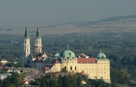 Luftaufnahme des Stifts Klosterneuburg mit zwei Kirchtürmen und umliegender Landschaft.