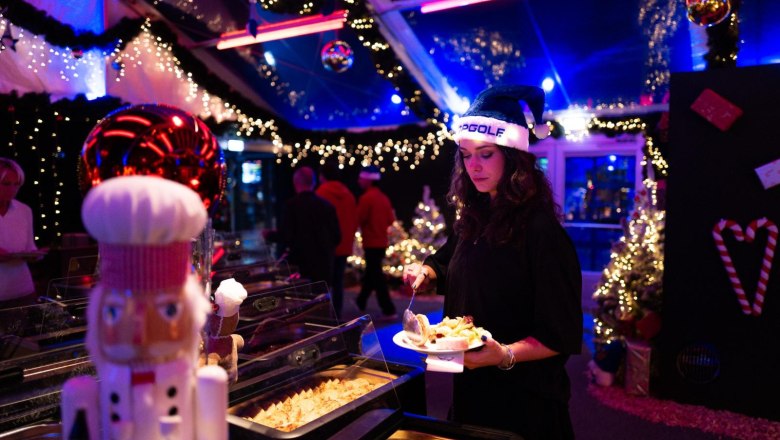 Stimmungsvoll beleuchtetes Winterevent bei Topgolf mit festlicher Dekoration, Weihnachtslichtern und Buffet in gem&uuml;tlicher Weihnachtsatmosph&auml;re.