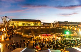 Weihnachtsmarkt im Schloss Hof bei D&auml;mmerung mit Lichtern und Menschen.